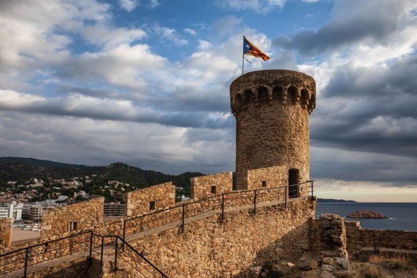 A stone tower with a flag, surrounded by a stone wall and a coastal landscape. 5