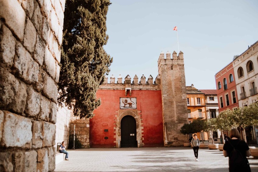 A historic red gate with a lion emblem, a tall tower, and a flag atop. 2