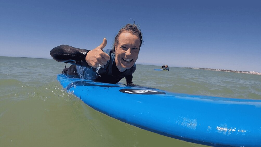 A person on a blue surfboard in the ocean, giving a thumbs-up. 1