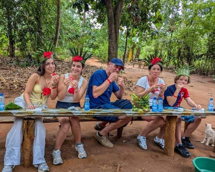 A group of people sitting at a table outdoors with greenery in the background. 3