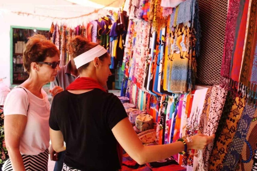Two people browsing colorful textiles at a market stall. 2