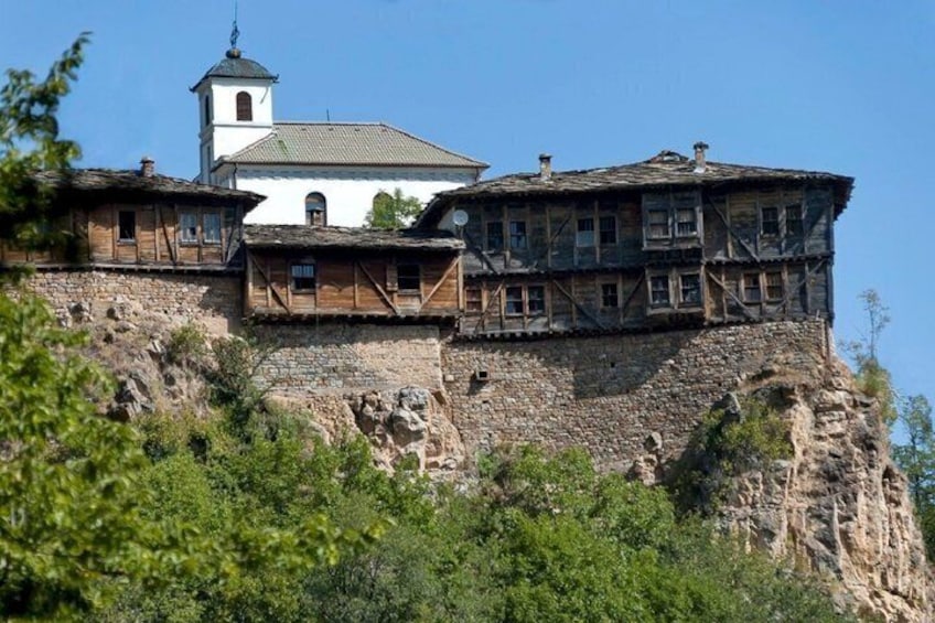 A historic building with a bell tower, wooden balconies, and a stone base on a hillside. 1