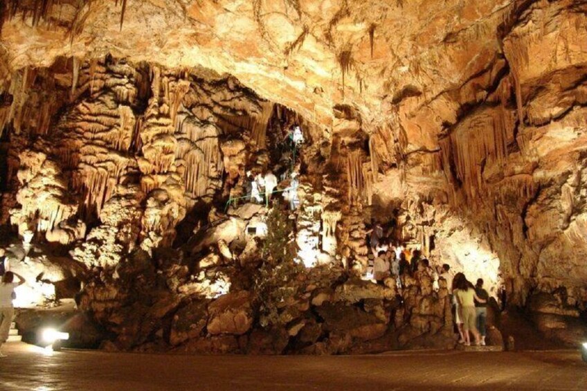 A cave with stalactites and stalagmites, illuminated by artificial lighting, with visitors exploring the formations. 5