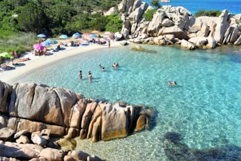 A clear turquoise sea, rocky formations, and people swimming and relaxing on the beach. 5