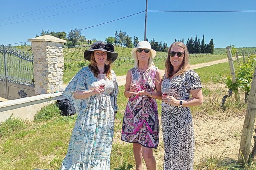Three people standing outdoors, one holding a drink, with a stone structure and a fence in the background. 1