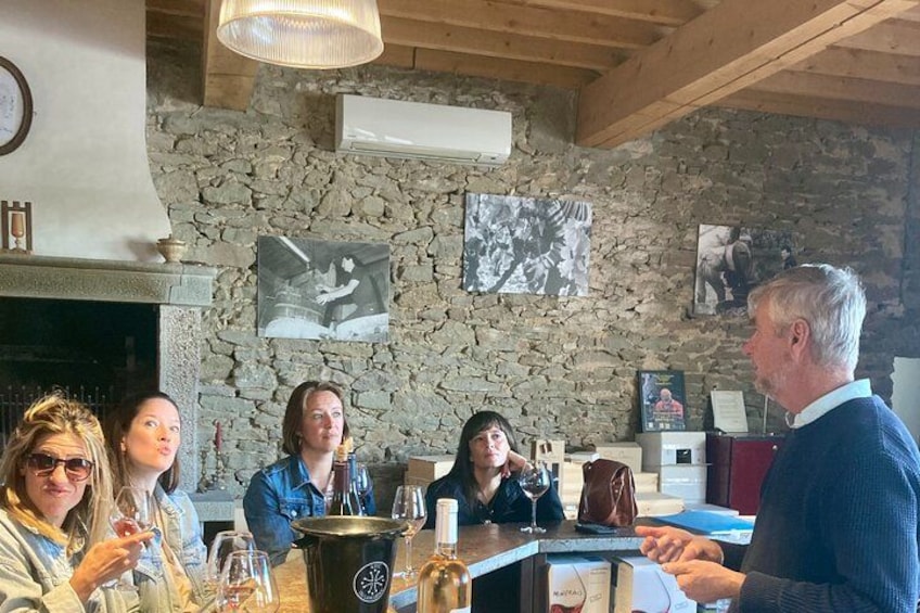 A group of people sitting around a table with wine glasses, a bottle of wine, and a bottle of water. There are pictures on the wall and a stone wall behind them. 3