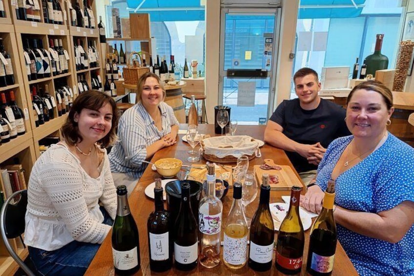 A group of people seated at a table with various bottles of wine and glasses. 3