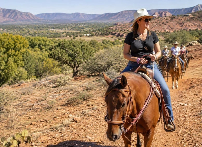 A person riding a horse along a dirt path with sparse vegetation and distant mountains. 5