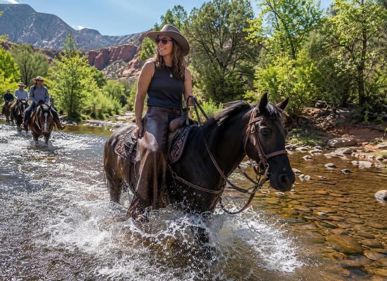A person riding a horse through a river with other riders in the background. 2