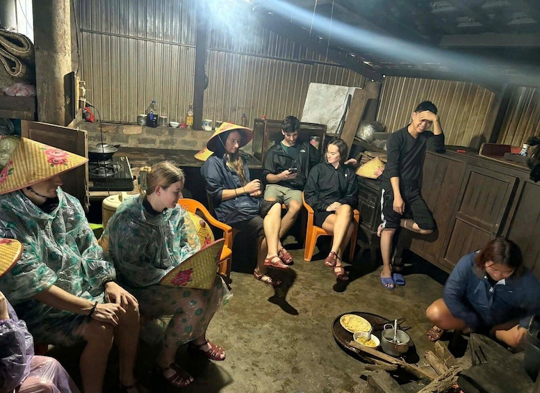 A group of people in a rustic indoor setting with wooden walls and a makeshift dining area. 1