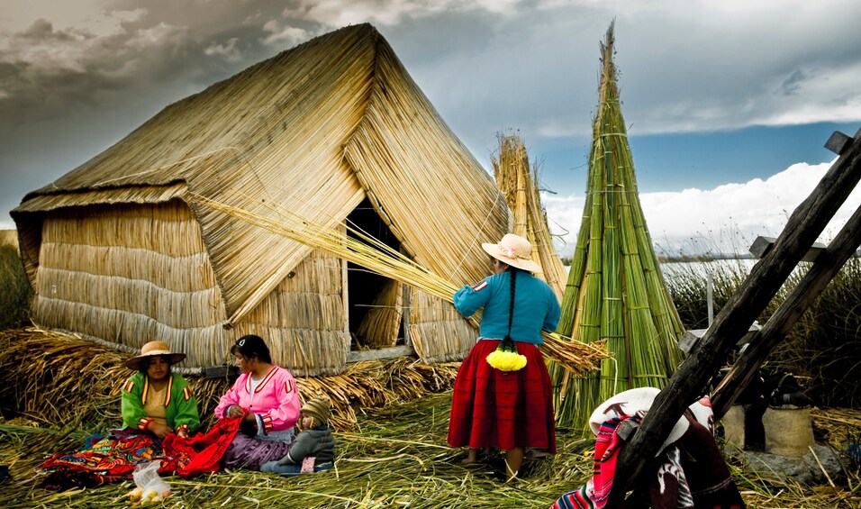 Three Uros women work in front of entirely thatched house in Peru