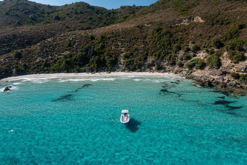 A boat on a turquoise sea with a sandy beach and green hills in the background. 1