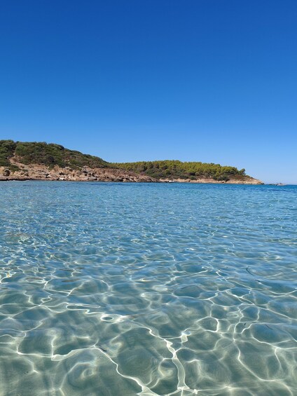 Clear shallow waters, a rocky coastline, and a forested hill. 2