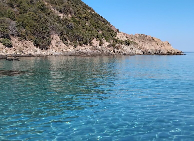 A clear coastal water body with a rocky hillside in the background. 5