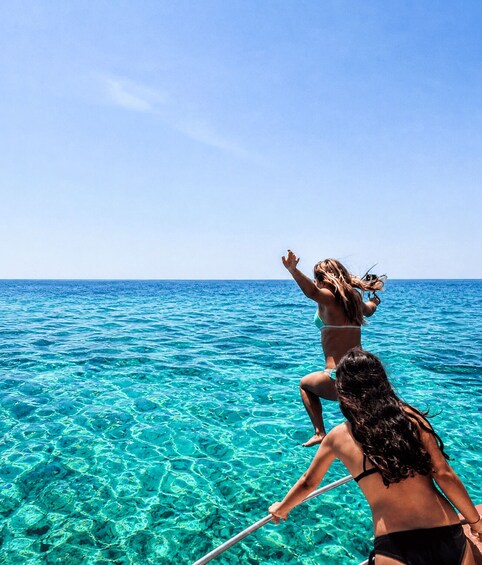 Two people in bikinis standing in clear turquoise water, with one person reaching towards the sky. 3