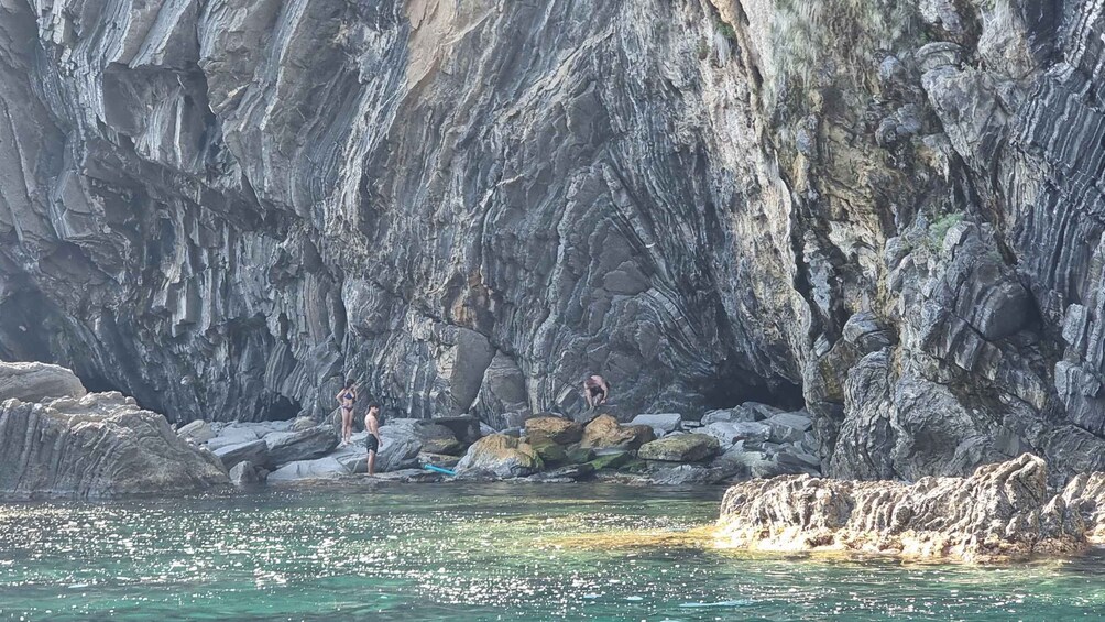A rocky coastline with clear water and people engaging in water activities. 3