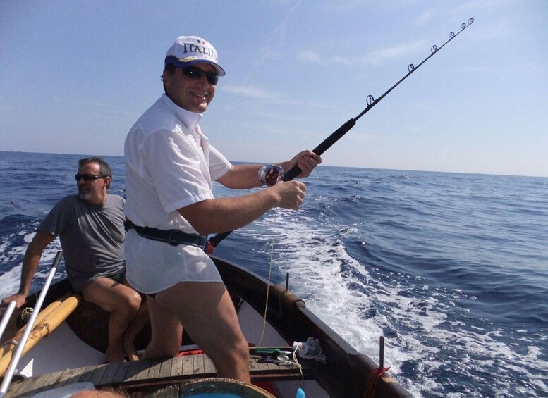 A person fishing on a boat with another person seated beside them. 2