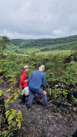 Two people examining a rocky terrain with lush greenery in the background. 3