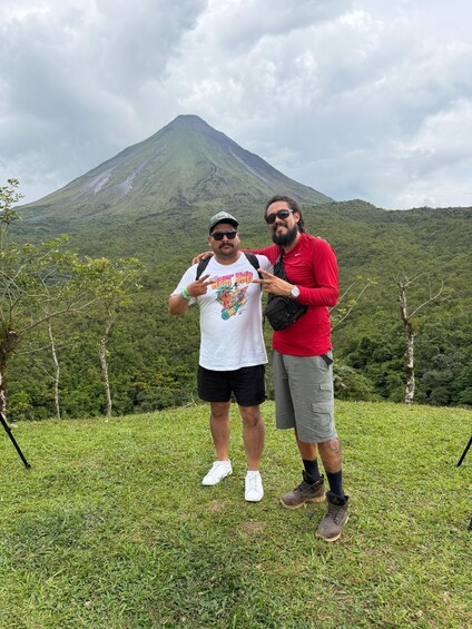 Two people standing on a grassy hill with a mountain in the background. 4