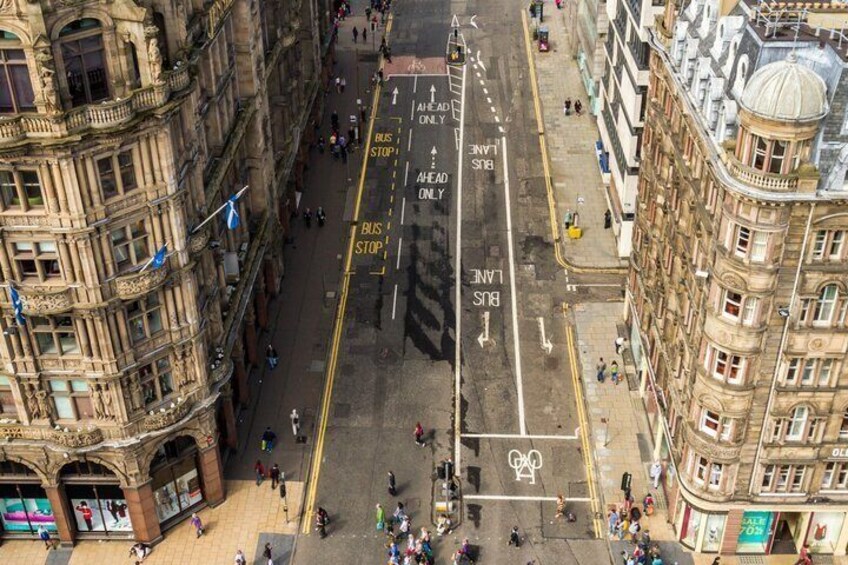 An aerial view of a city street with historic buildings, a bus stop, and a pedestrian crossing. 4
