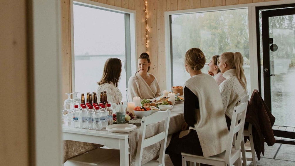 A group of people seated at a table with food and drinks, in a room with large windows and a view of the outdoors. 2