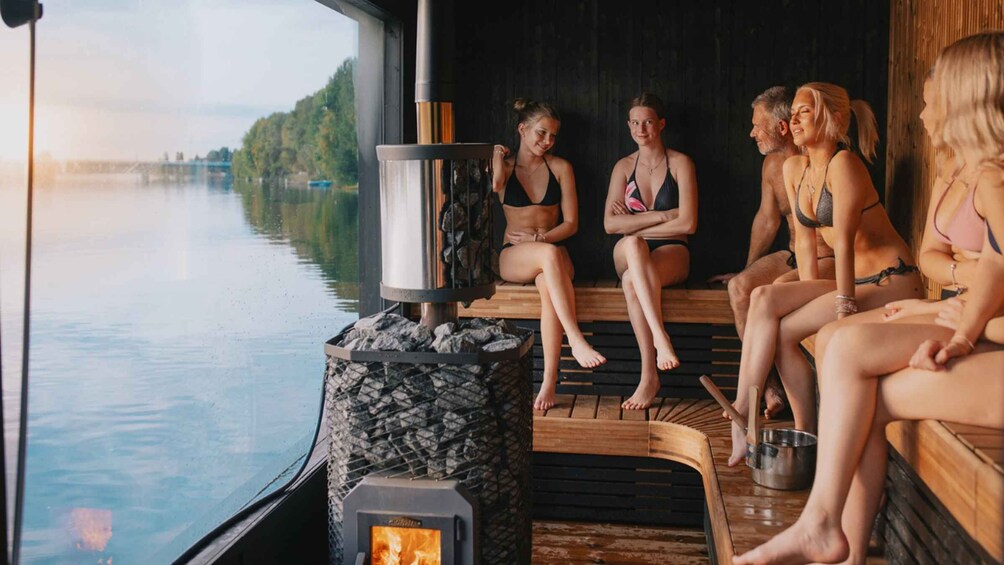 A group of people in swimwear sitting by a wood-fired sauna on a boat. 1