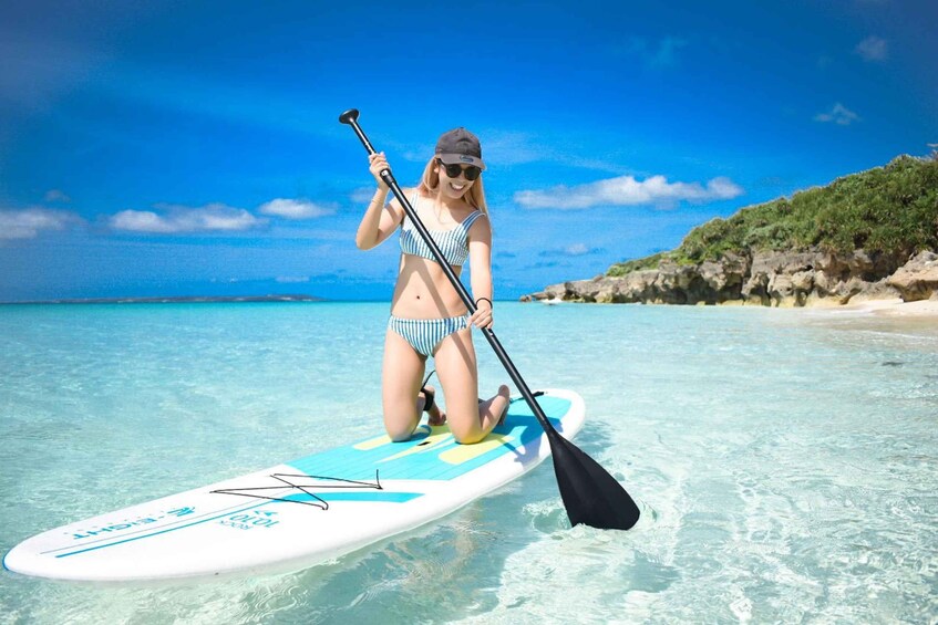 A person paddleboarding on clear turquoise water with a rocky coastline in the background. 2