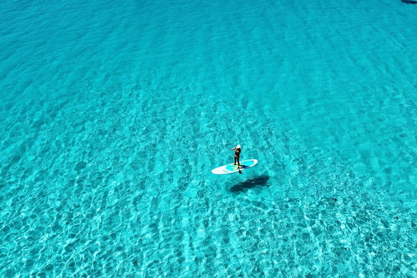 A person standing on a surfboard in clear turquoise water. 3