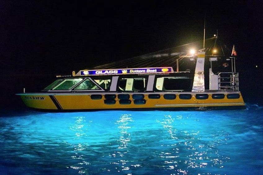 A yellow and black boat named 'Sea View' with 'Glass Bottom Boat' signage, floating on water at night. 2