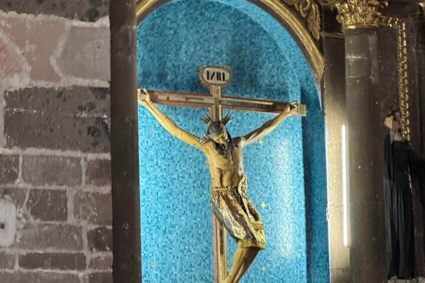 A crucifixion scene with a figure on the cross, a blue mosaic background, and a column with a cross on top. 1