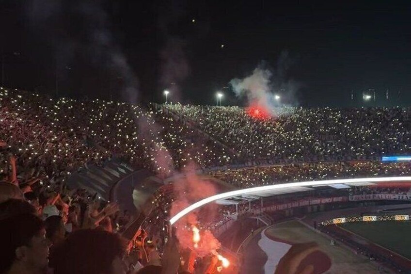 A stadium filled with spectators, a large crowd, and a stage with lighting. 3