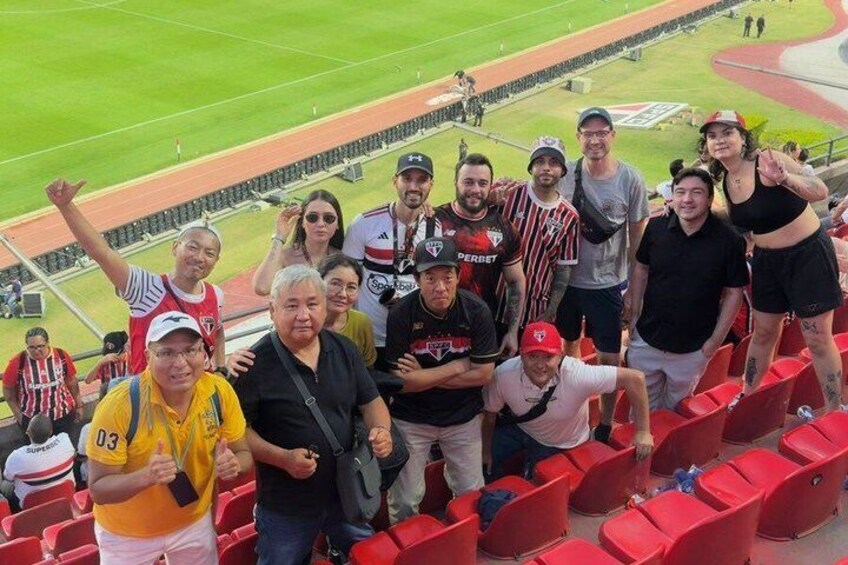 A group of people at a sports stadium with red seating and a track. 1