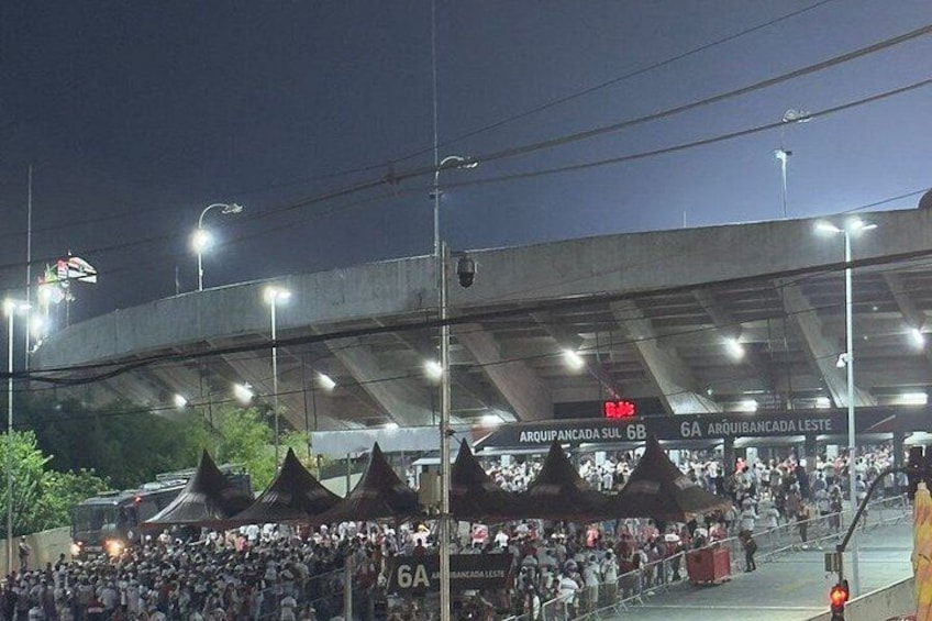 A stadium with a crowd, a covered walkway, and signage for entrances. 3