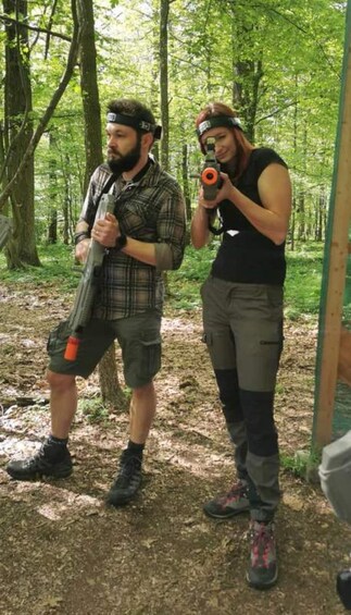 Two people in a forest holding paintball guns. 1