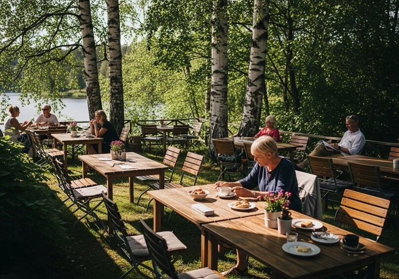 Ulkoterassi, jossa on puupöytiä ja -tuoleja, ja jota ympäröivät koivupuut ja järvi. 3