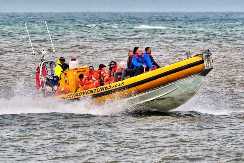 A yellow speedboat with passengers wearing life jackets on the water. 1