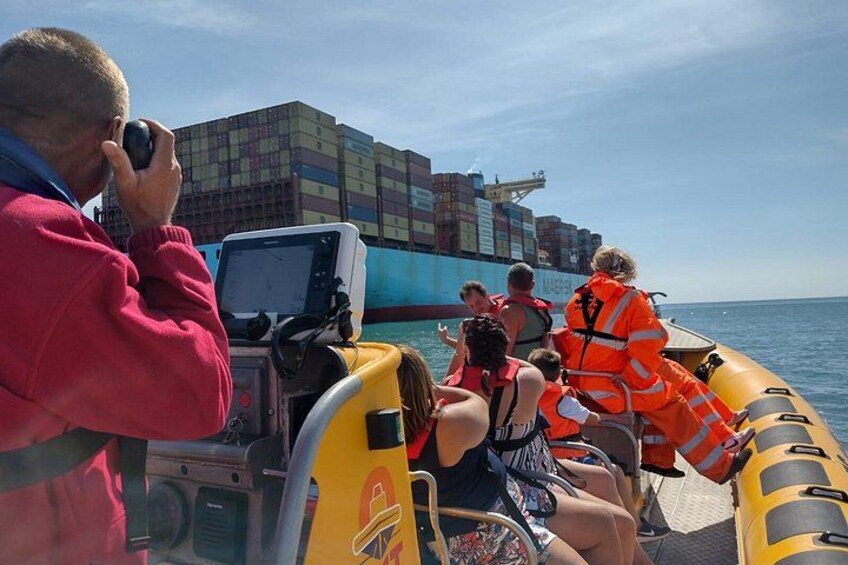 A group of people on a boat near a large cargo ship. 3