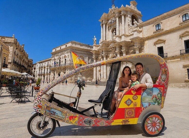 A colorful rickshaw with passengers, parked in a plaza with historic architecture. 2