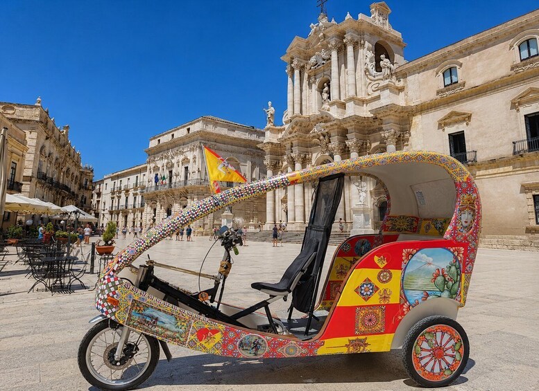 A colorful rickshaw parked in a plaza with ornate buildings in the background. 3