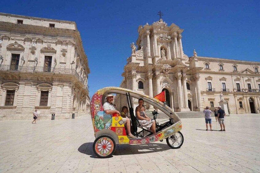 A colorful rickshaw with passengers in front of a grand historical building. 1