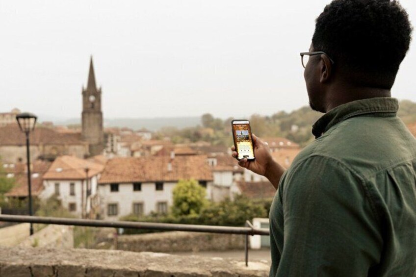 A person taking a photo of a town with a prominent church tower. 1