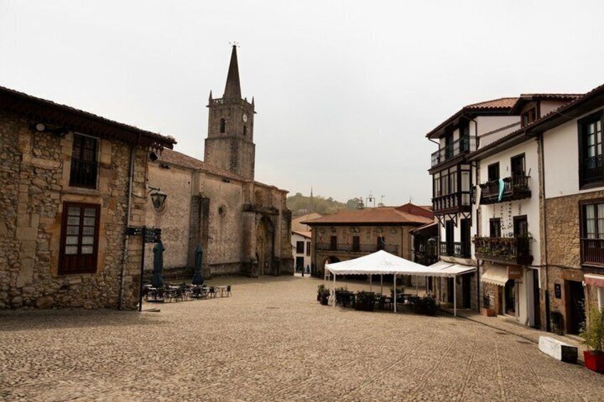 A cobblestone square with historic buildings, a church tower, and outdoor seating. 2