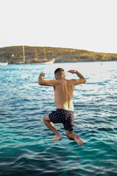 A person jumping into the water with a boat and a hilly landscape in the background. 3