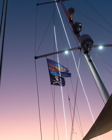 A sailboat's rigging with flags, including a 'Sailors' Paradise' banner and a skull and crossbones flag. 2