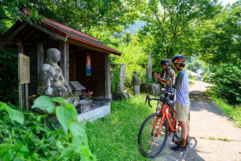 A wooden shrine with a statue, surrounded by lush greenery and a path. 3