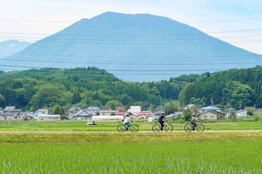 Three cyclists on a rural road with houses and a mountain in the background. 4