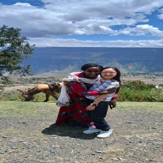 Two people standing on a rocky outcrop with a mountainous landscape in the background. 3
