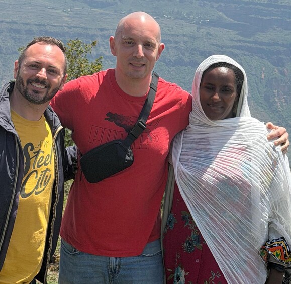 Three people standing on a mountain with a valley in the background. 1