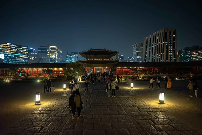A traditional building with a pagoda-style roof, surrounded by modern high-rise buildings, in a public square with people walking and street lamps. 5