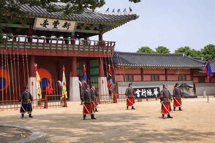 A traditional Korean gate with guards in uniform, flags, and a sign with Korean characters. 1